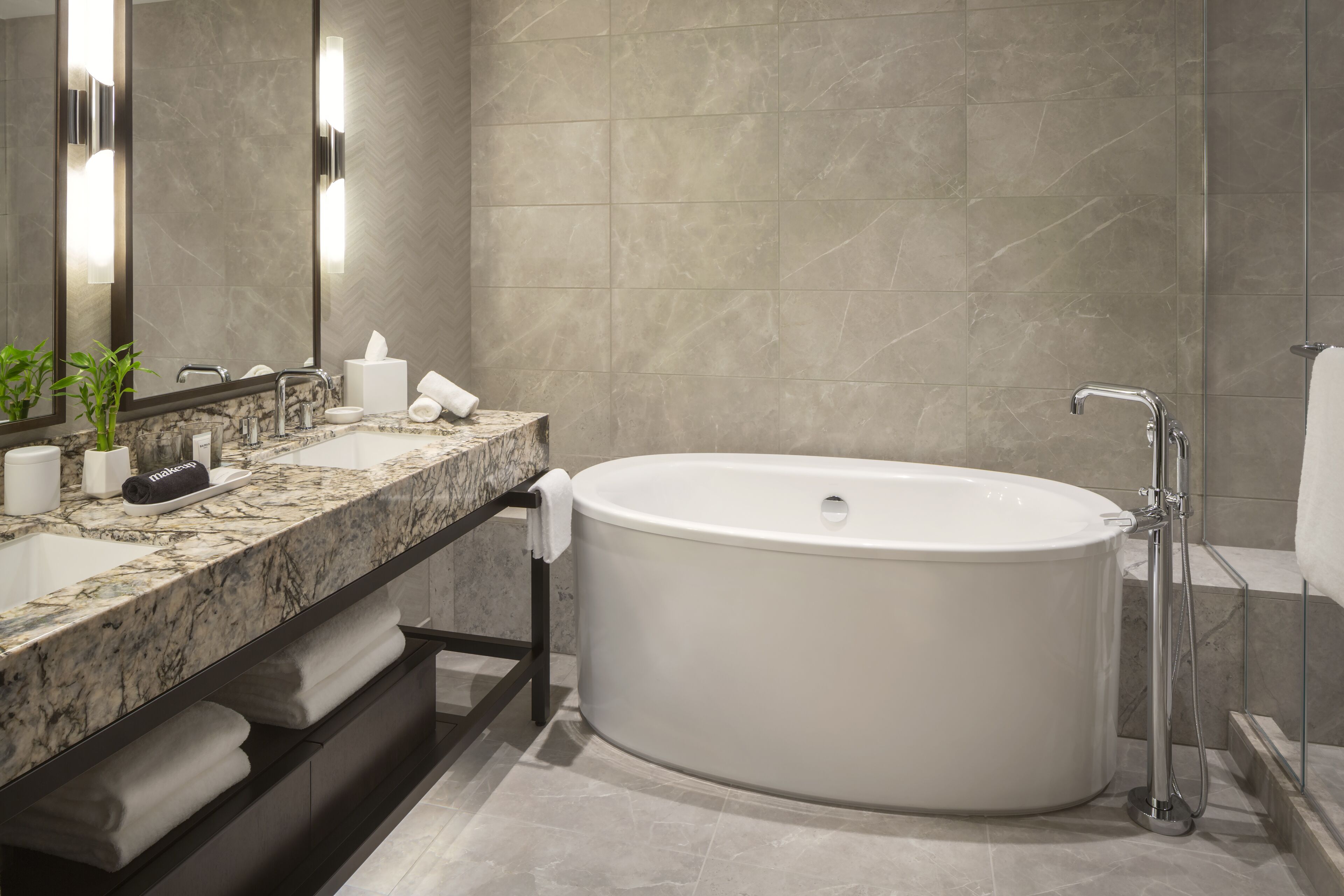 A modern bathroom with a freestanding bathtub, a marble sink, and a large mirror.