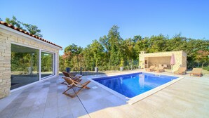 A modern outdoor pool area with a stone building, lounge chairs, and a clear view of the surrounding trees. - Villa Adrimar (Vrbnik)