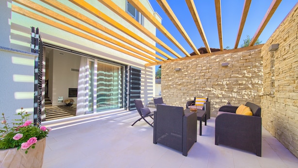 An outdoor patio with wicker furniture, a stone wall, and a wooden pergola. - Villa Adrimar (Vrbnik)