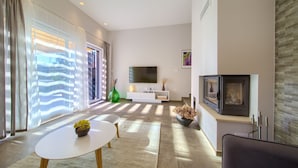 A modern living room with a flat-screen TV, a fireplace, and a large window with curtains. - Villa Adrimar (Vrbnik)