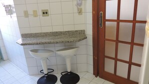 A bathroom with two white pedestal sinks, a granite countertop, and a wooden door with glass panels. - Praia das Dunas Apartamento Aconchegante 2 Quartos (Cabo Frio)