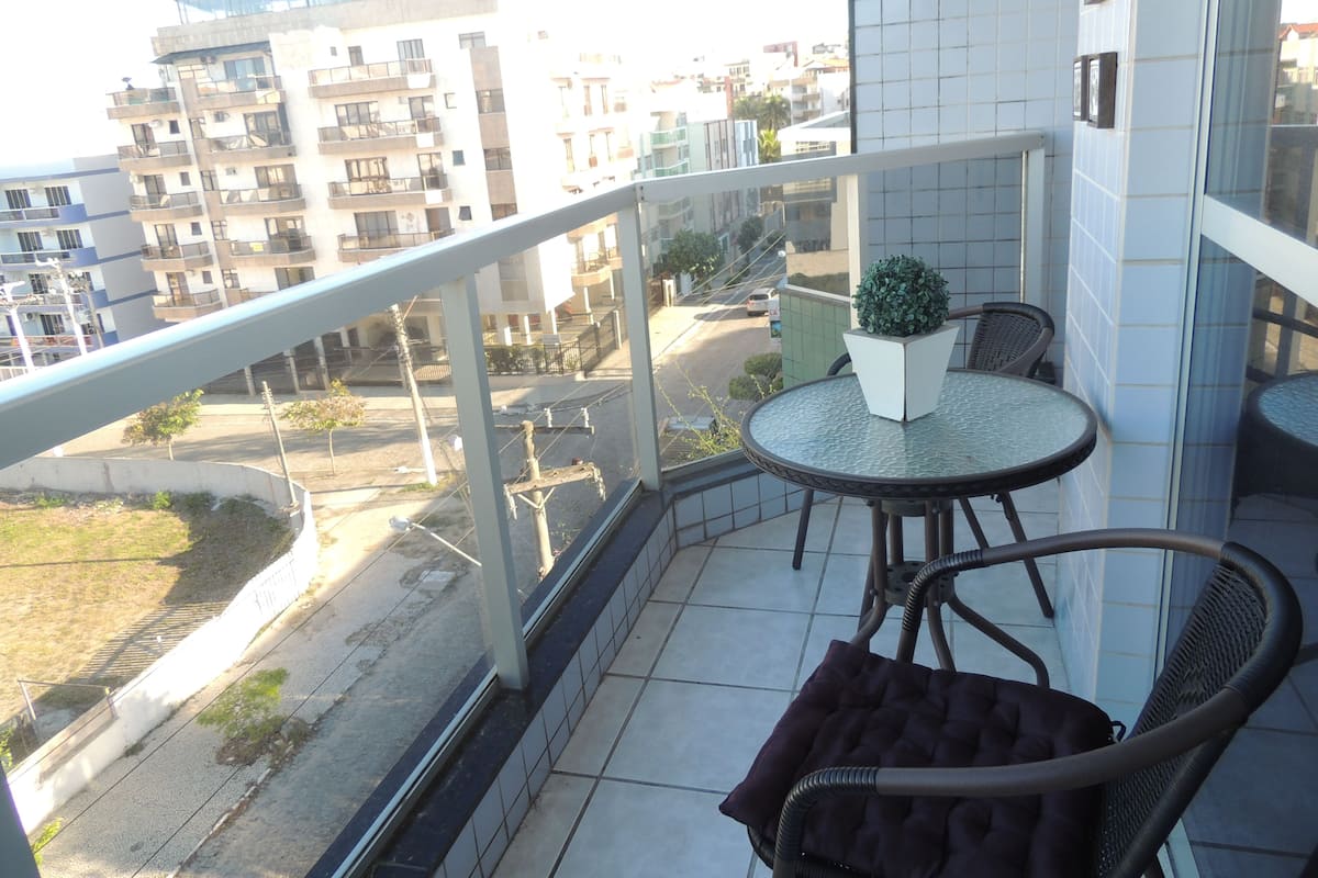 A balcony with a round table, two chairs, a potted plant, and a view of surrounding buildings.