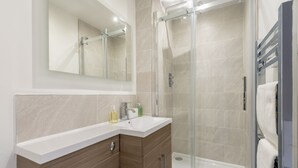 Un baño moderno con cabina de ducha de vidrio, lavamanos blanco y tocador de madera.