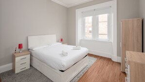 Un dormitorio con cama, mesitas de noche, cómoda y ventana.