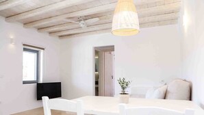 A bright, modern room with a white dining table, white chairs, a ceiling fan, and a hanging light fixture. - VLIA MAR Myconian Residences (Mykonos)