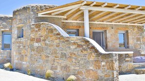 A stone building with a wooden pergola, windows, and a curved wall. - VLIA MAR Myconian Residences (Mykonos)