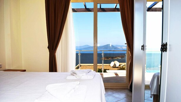 A hotel room with a bed, a sliding glass door leading to a balcony with a view of the sea and mountains.