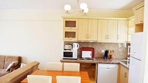 A compact kitchen with wooden cabinets, a granite countertop, a microwave, a kettle, and a dishwasher.