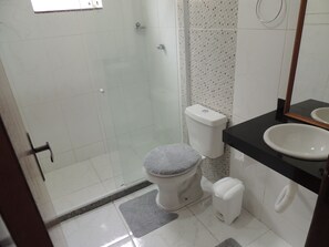 A bathroom with a glass shower enclosure, a toilet, a sink, and a mirror.