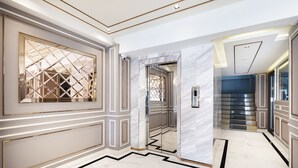 Un hall d’entrée luxueux, doté d’un sol en marbre, de miroirs encadrés d’or et d’un escalier moderne.