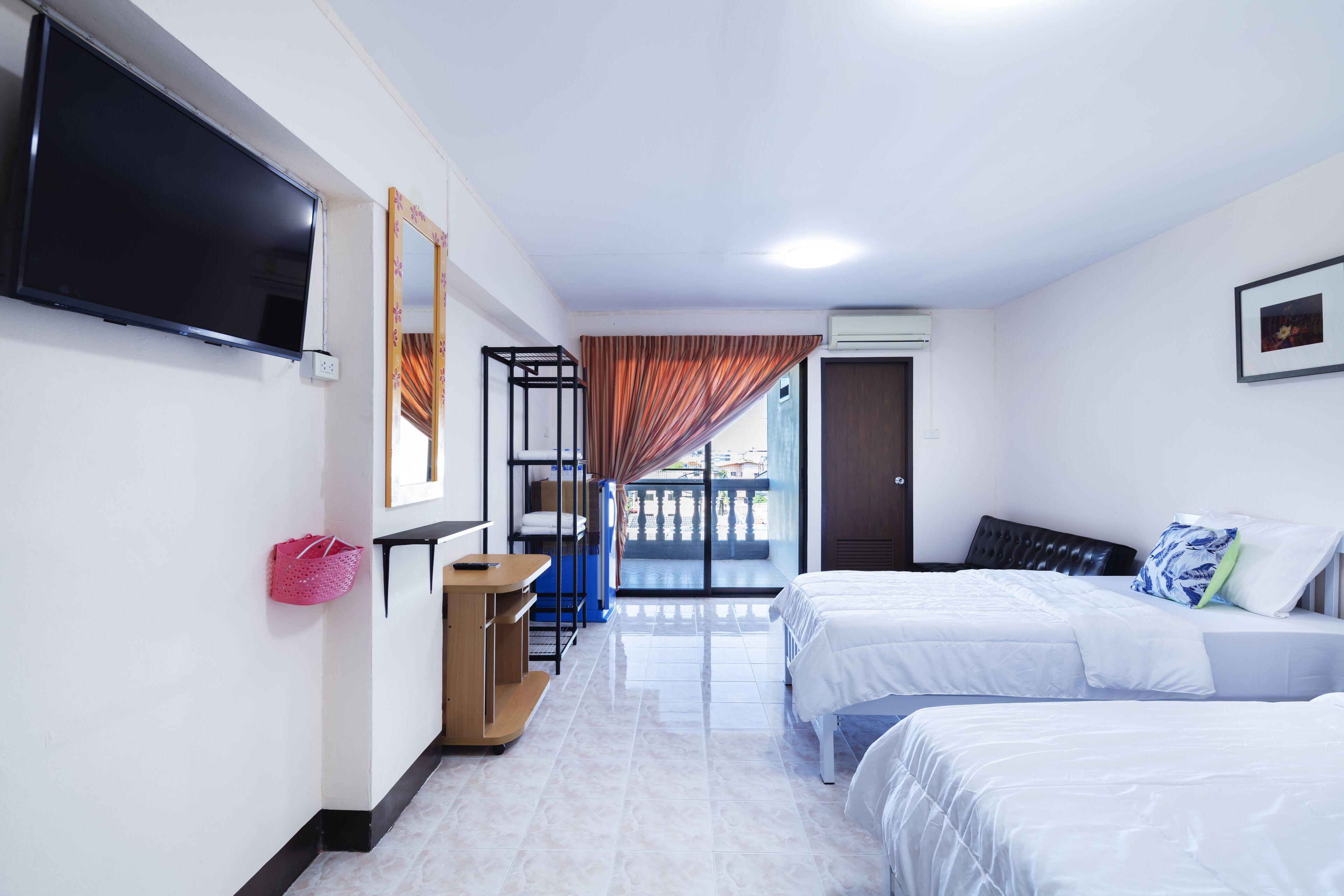A hotel room with two beds, a TV, a desk, and a balcony with curtains.