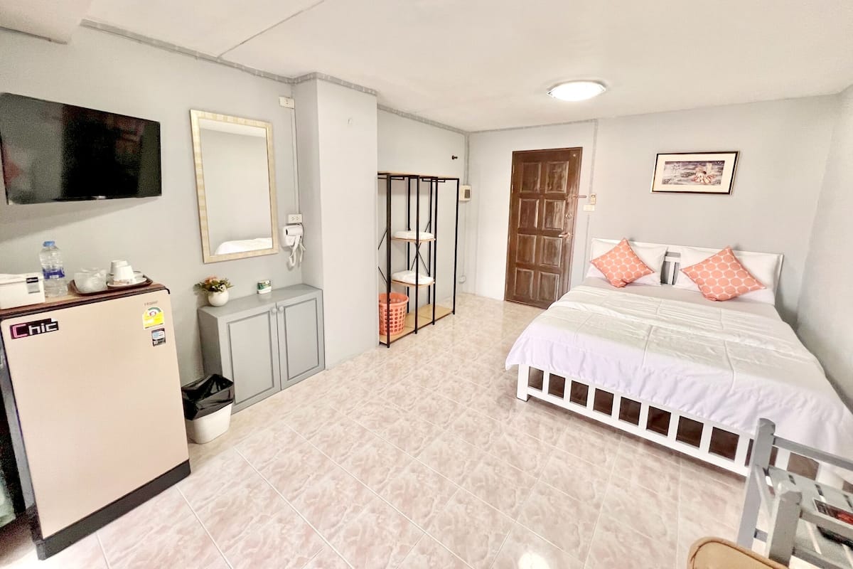 A hotel room with a bed, a wardrobe, a desk with a refrigerator, a television, and a door leading to another room.