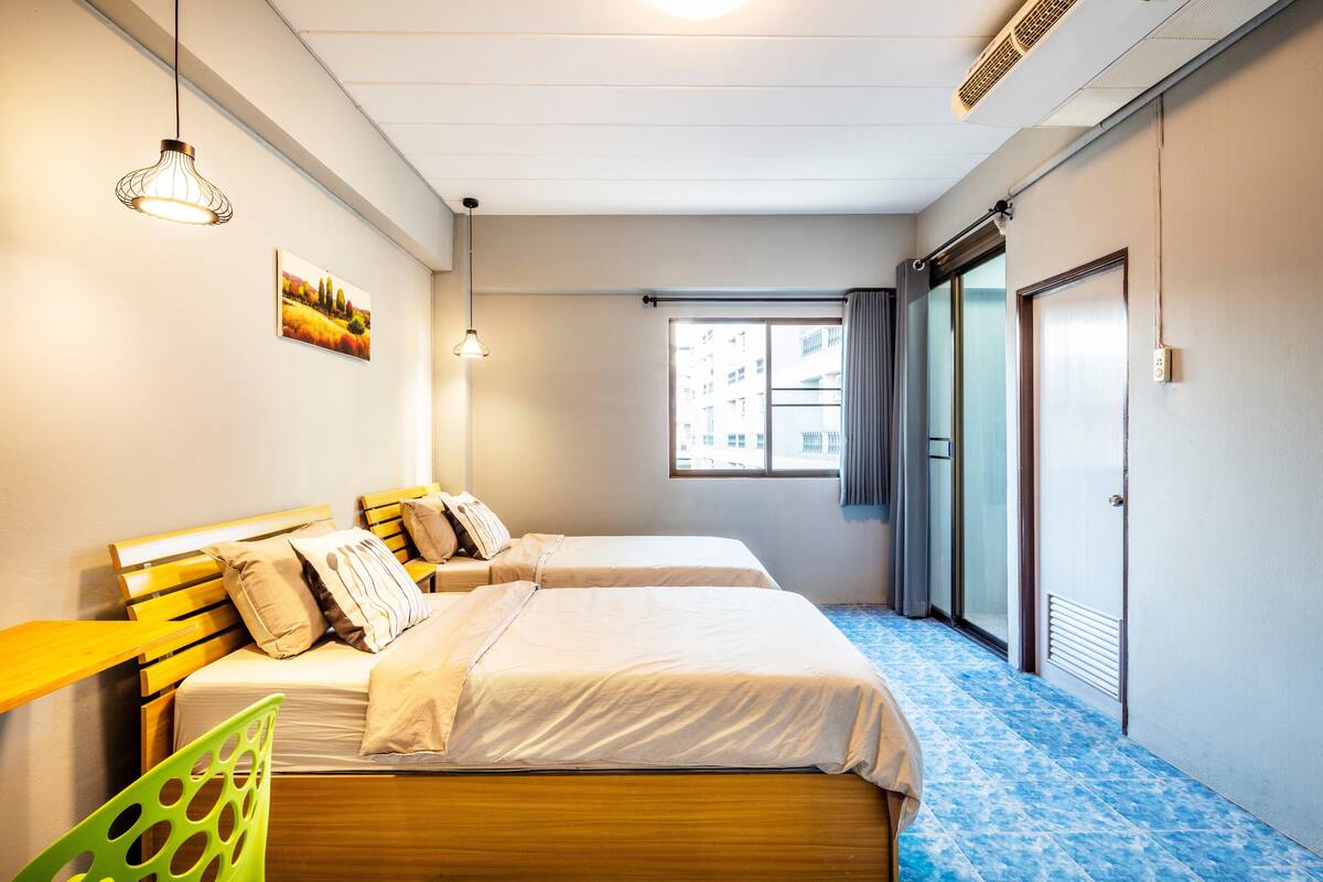 A hotel room with two beds, a window with a view, a door, and a green chair.