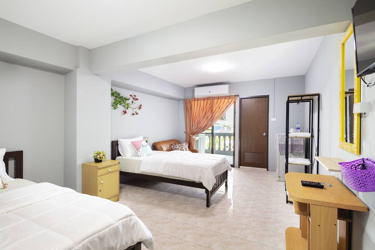 A bedroom with two beds, a desk, a chair, a TV, and a window with curtains.