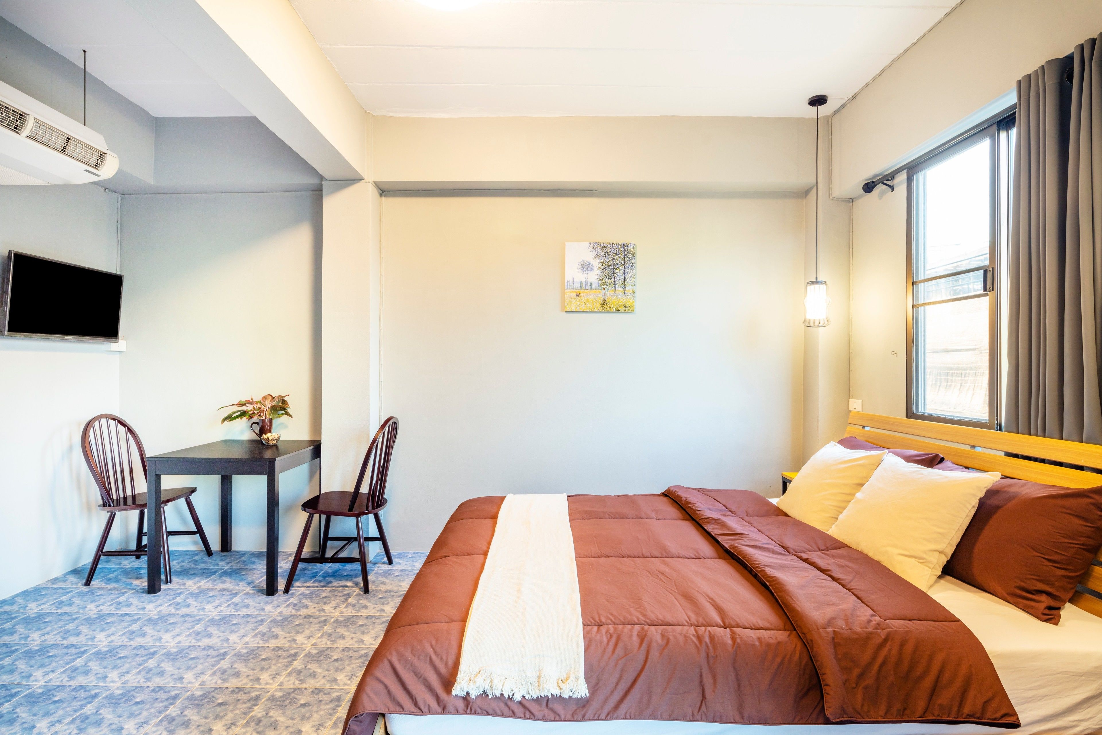 A hotel room with a bed, a desk with chairs, a TV, and a window with curtains.