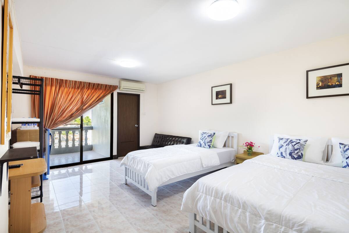 A hotel room with two beds, a desk, a chair, a window with curtains, and a door.
