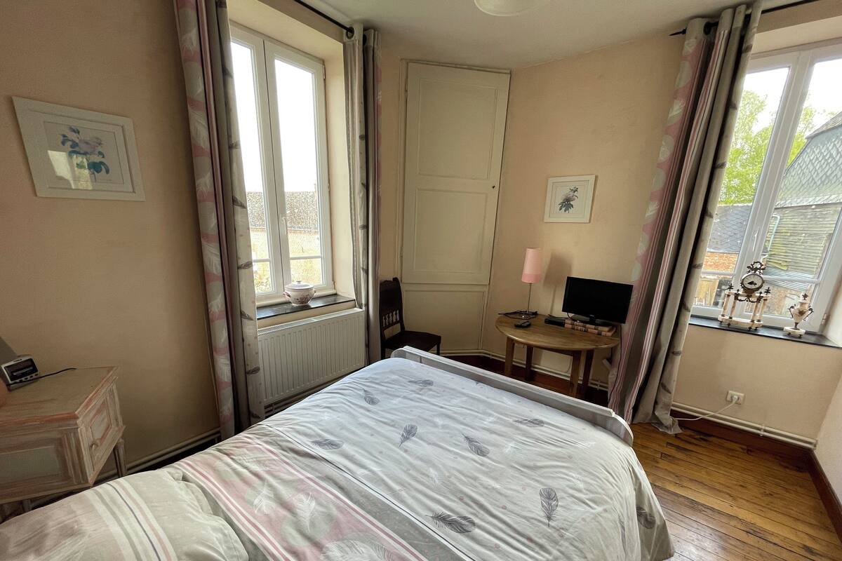 A bedroom with a bed, a desk, a chair, a small table with a lamp, and a television.
