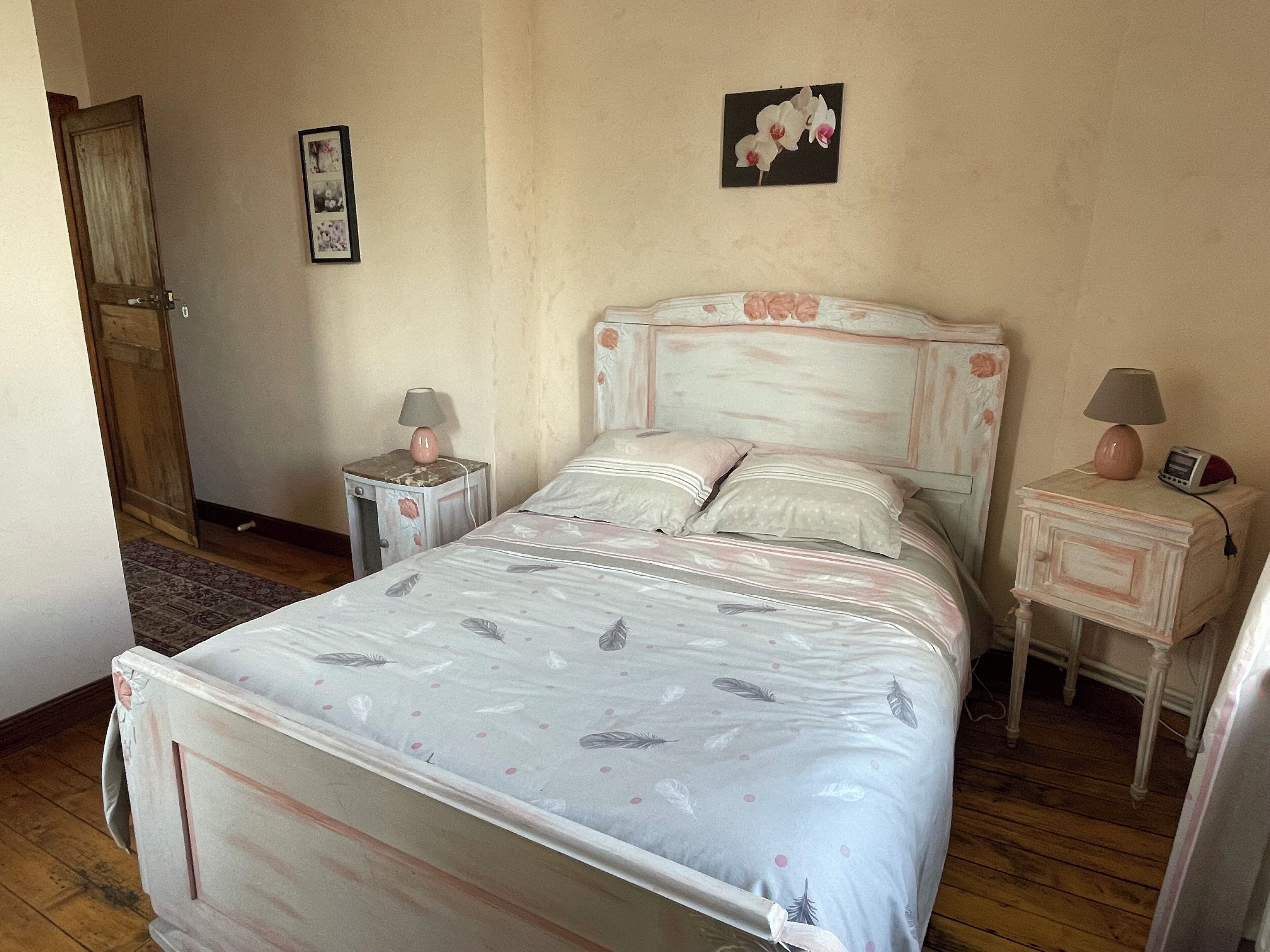 Un dormitorio con cama, dos mesitas de noche, un aparador, una puerta y una pared con un cuadro.