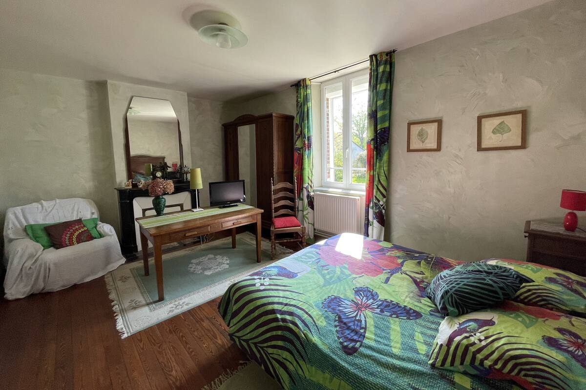A bedroom with a bed, a desk, a chair, a wardrobe, a mirror, and a window with curtains.