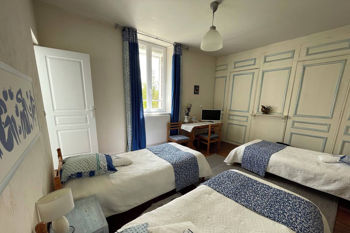 A bedroom with three beds, a desk with a computer, a chair, and a window with curtains.