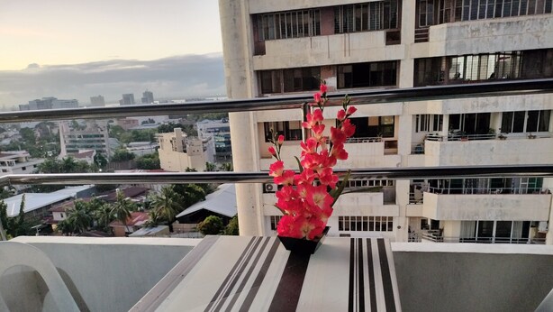 A balcony with a table and chairs, a vase with flowers, and a cityscape view in the background.