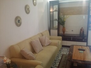 A living room with a yellow sofa, a wooden coffee table, and decorative wall mirrors. - Obaid's Condo in Winland Towers (Cebu City)