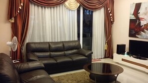 A living room with a black leather sofa, a glass coffee table, a flat-screen TV, and a fan.