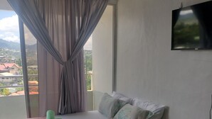 A bedroom with a bed, a TV on the wall, and a view of buildings through the window.