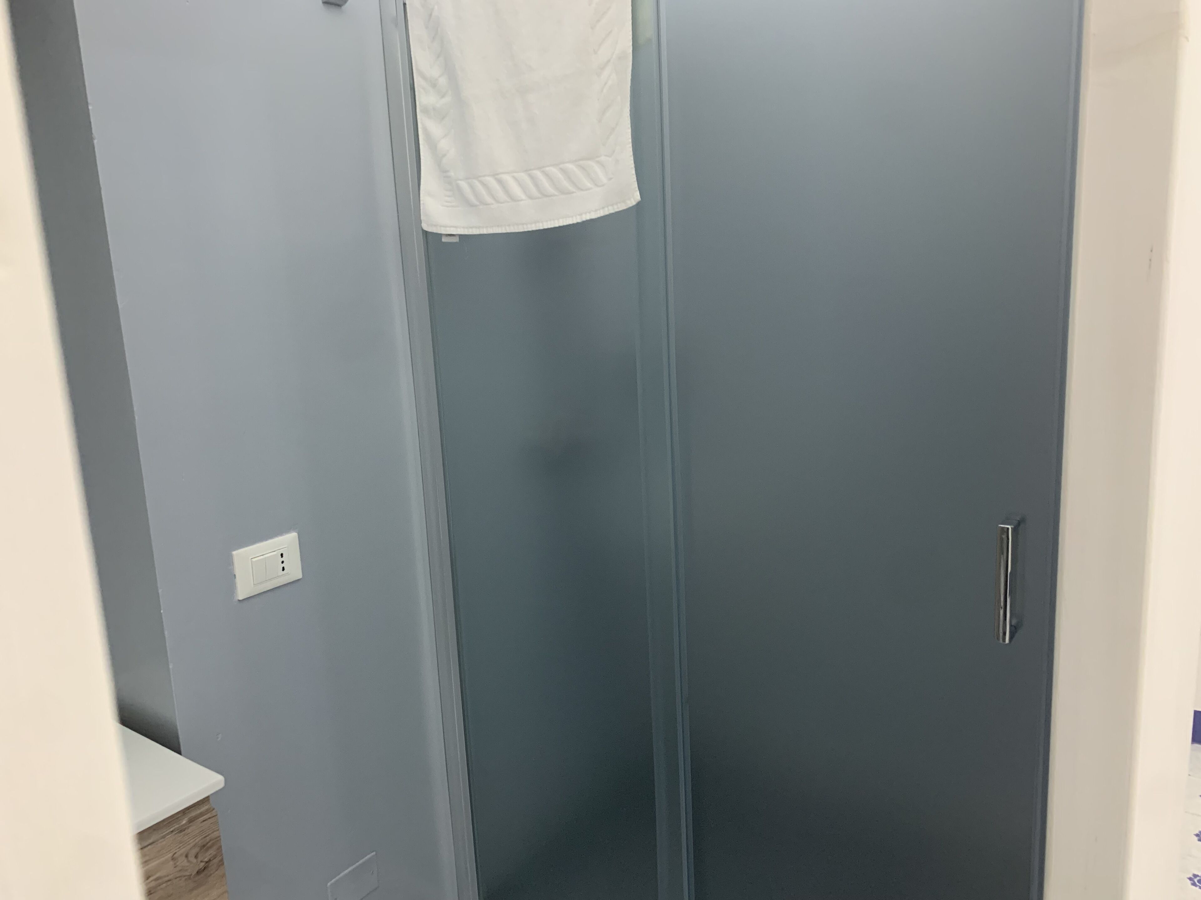 A bathroom with a grey door, a white towel hanging on the door, and a white countertop with a wooden base.