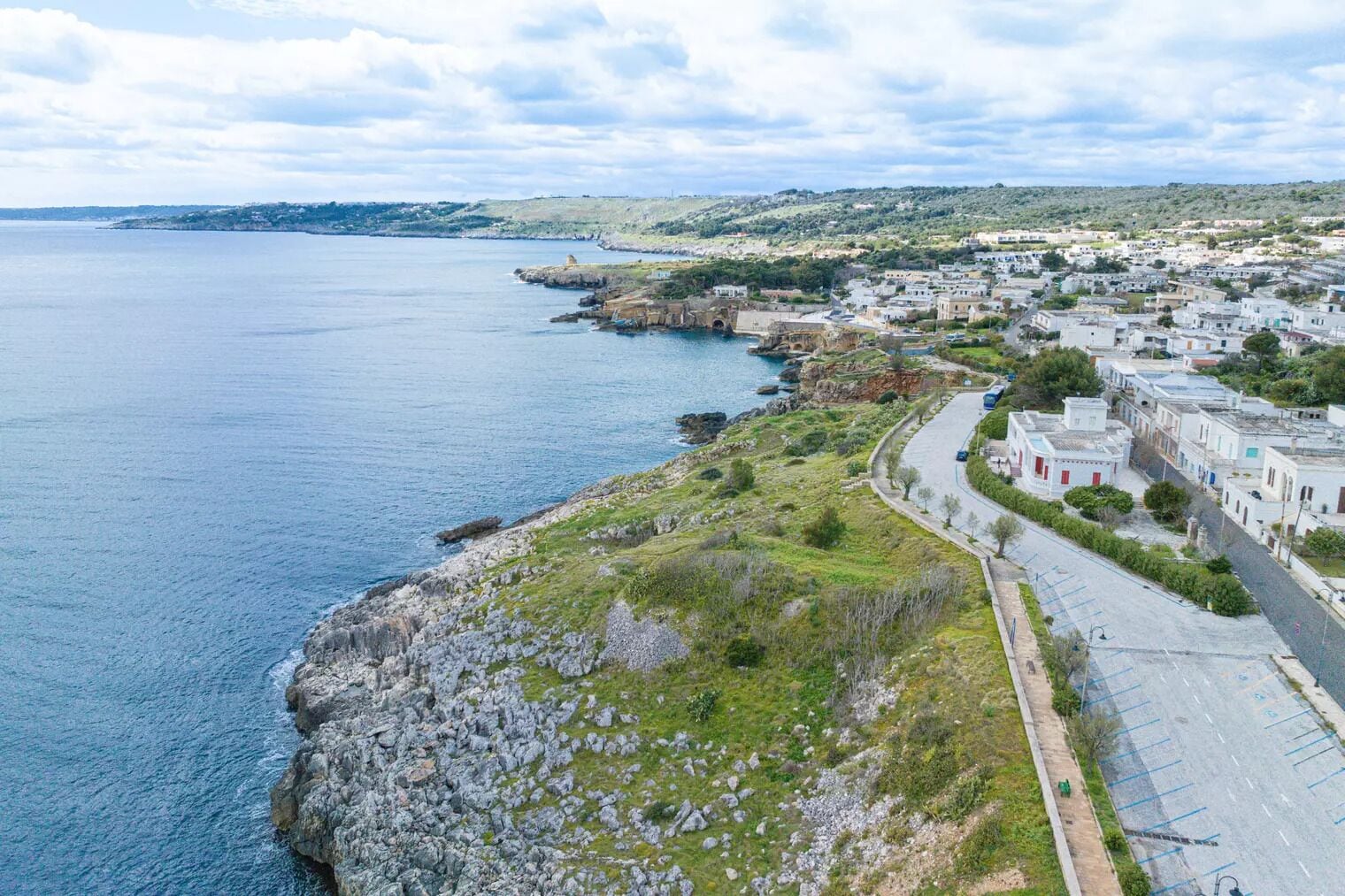 A coastal town with a rocky shoreline, a paved road, and buildings with a uniform architectural style.