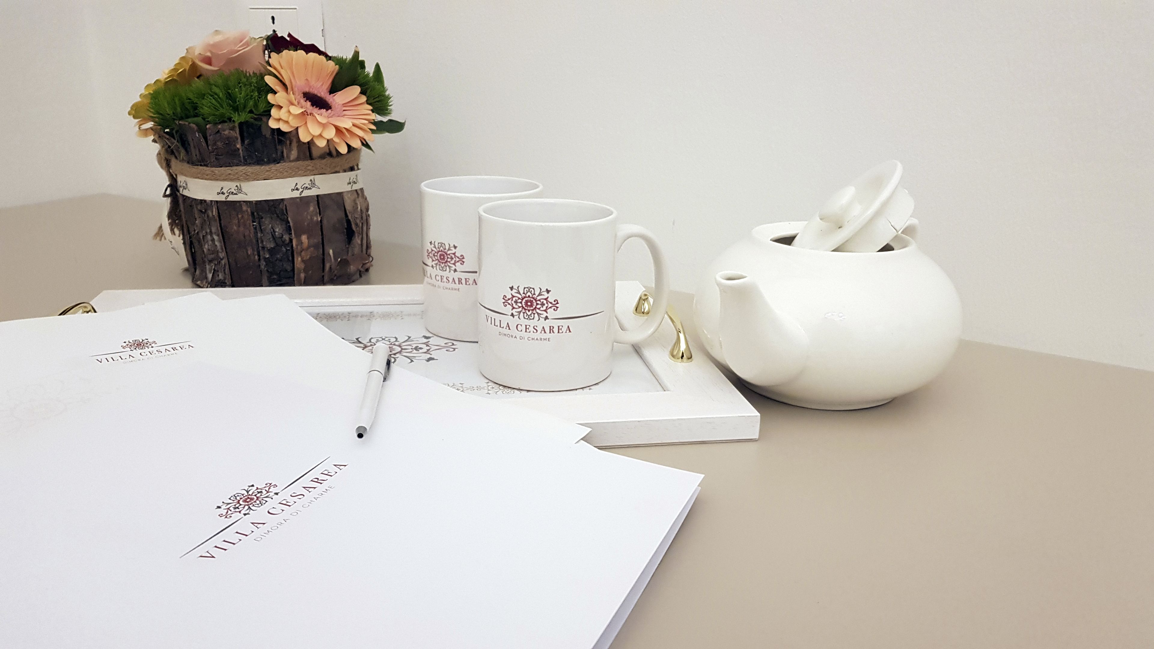 Ein Tisch mit einem weißen Teekessel, zwei weißen Tassen, einem Stift und einer dekorativen Vase mit Blumen.