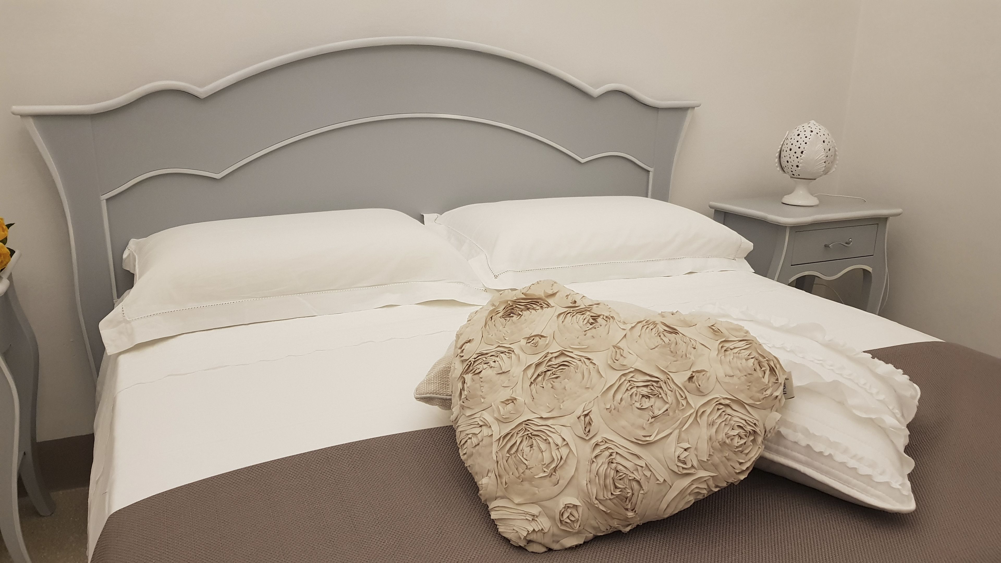 A bed with white bedding and a decorative pillow with a floral pattern.