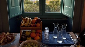 Una mesa con una exhibición de frutas, un tazón de uvas y vista al mar a través de una ventana.