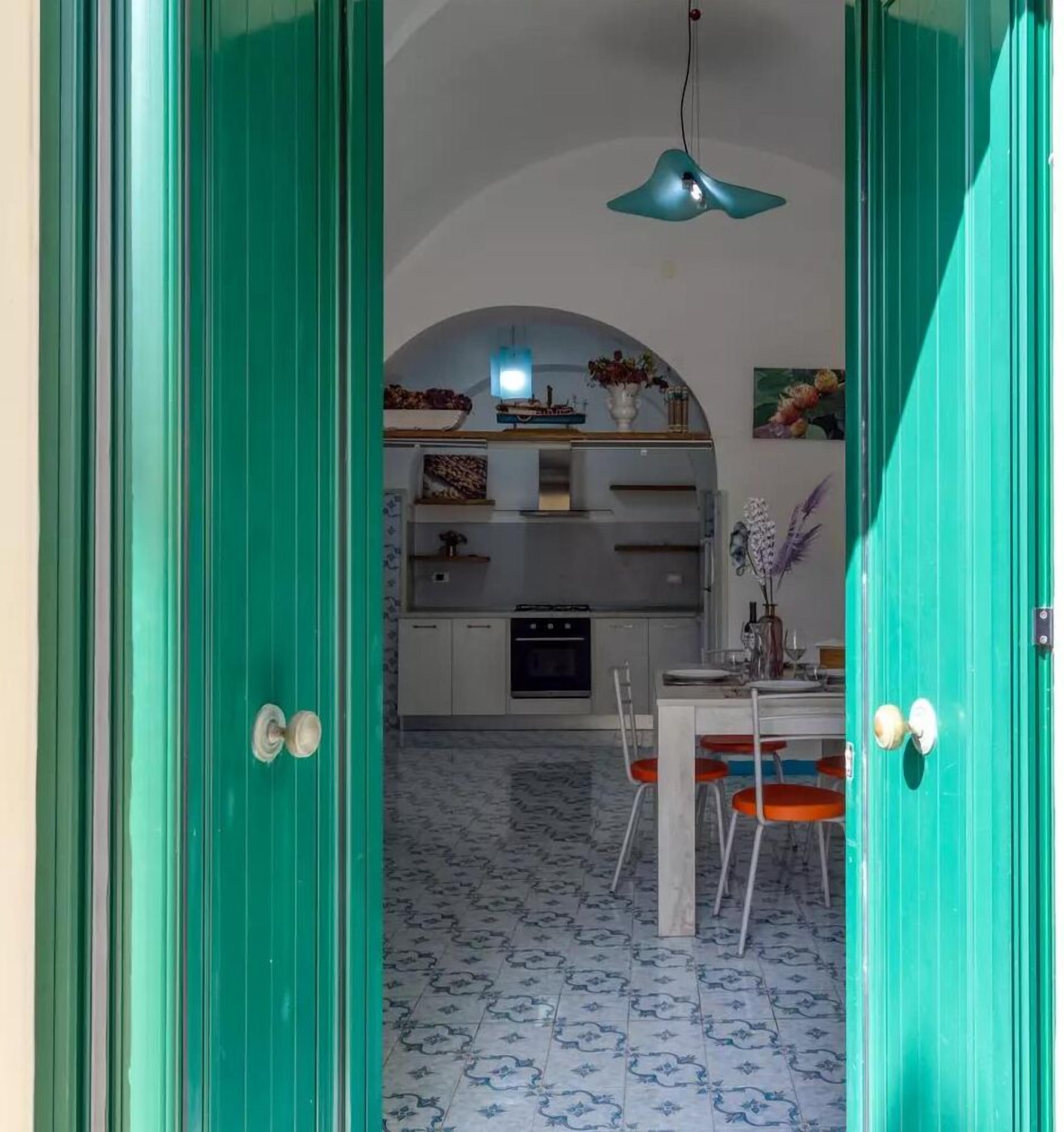 Una cocina con encimera blanca, lámpara colgante y comedor con mesa blanca y sillas naranjas.
