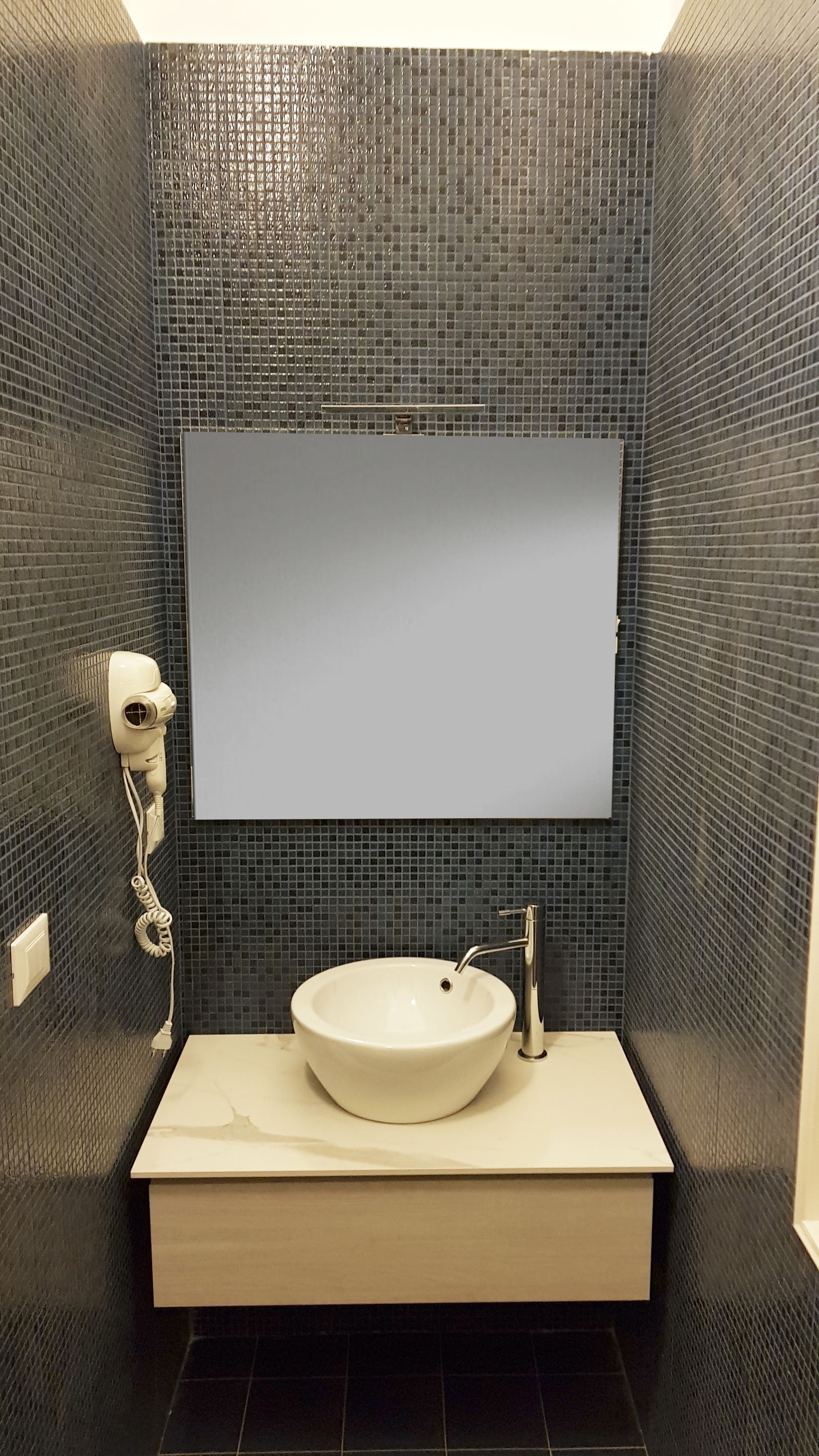 Ein Badezimmer mit einem weißen Waschbecken, einem Spiegel und einem Fön an der Wand.