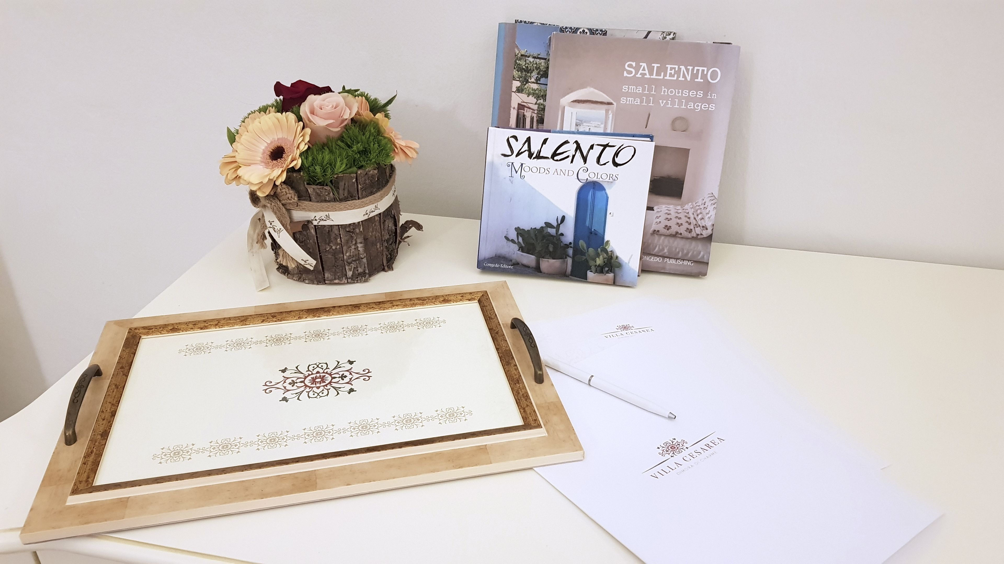 Een lijstwerk met een bloemenmotief, een boek getiteld 'SALENTO' en een notitieboekje op een tafel.