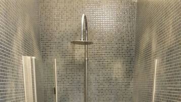 A small, enclosed shower stall with a glass door, a white toilet, and a tiled floor.