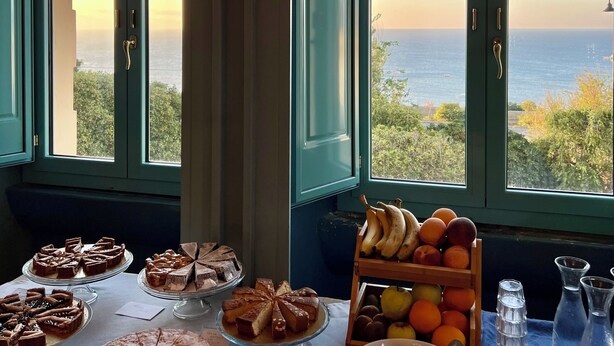 Una mesa con postres y fruta en una habitación con ventanas amplias que dan a un paisaje pintoresco.