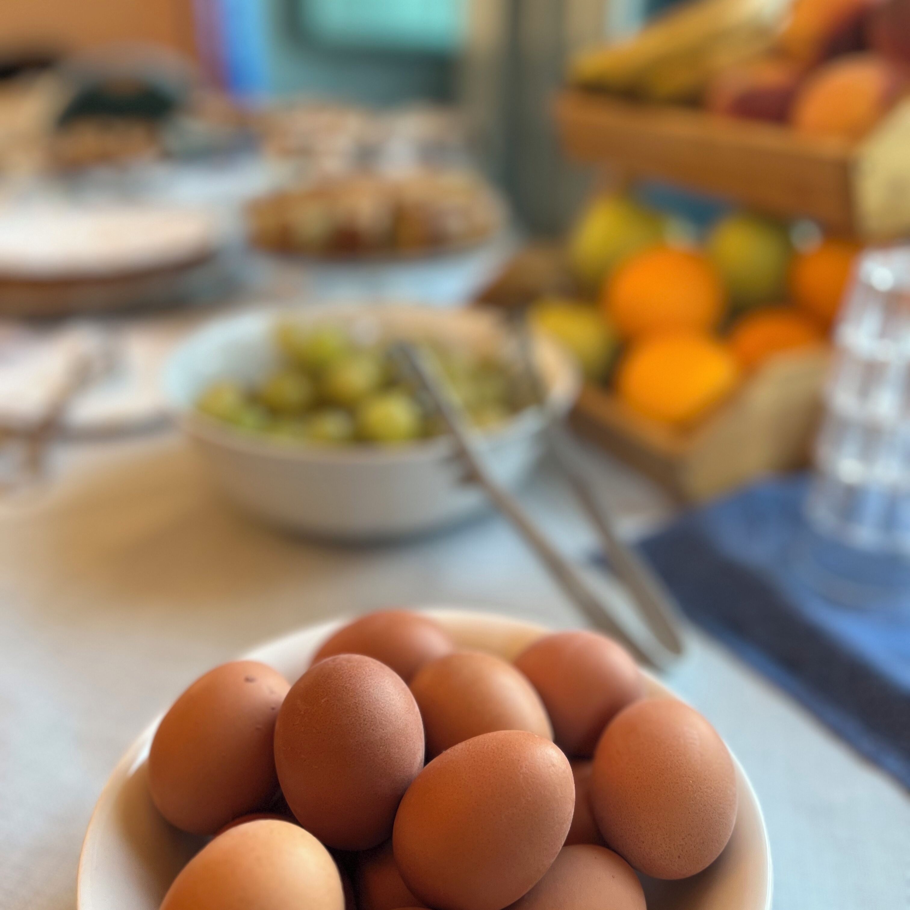 Une assiette d’œufs est posée sur une table, avec un bol de fruits et un panier de fruits en arrière-plan.