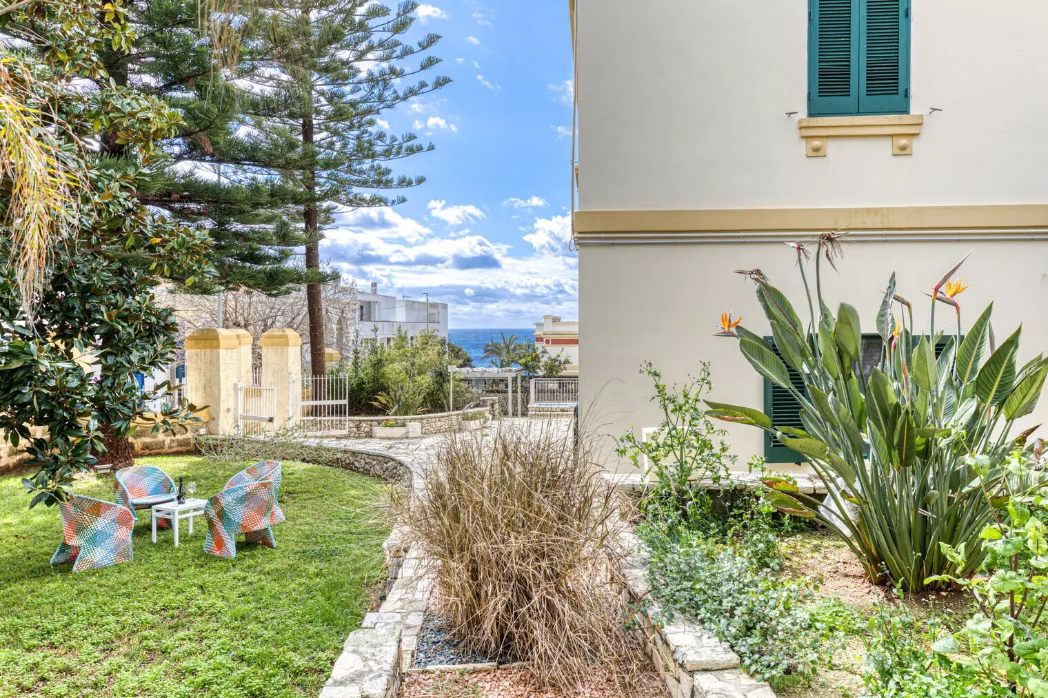 A garden with outdoor seating, a view of the sea, and a building with a balcony.