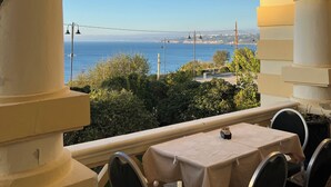 Un balcón con mesa y sillas, con vistas a la costa y un puente a lo lejos.