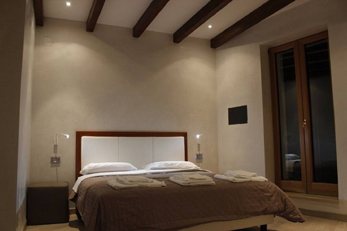 Un dormitorio con cama, lámparas de noche, techo de madera y puerta de vidrio corredera.