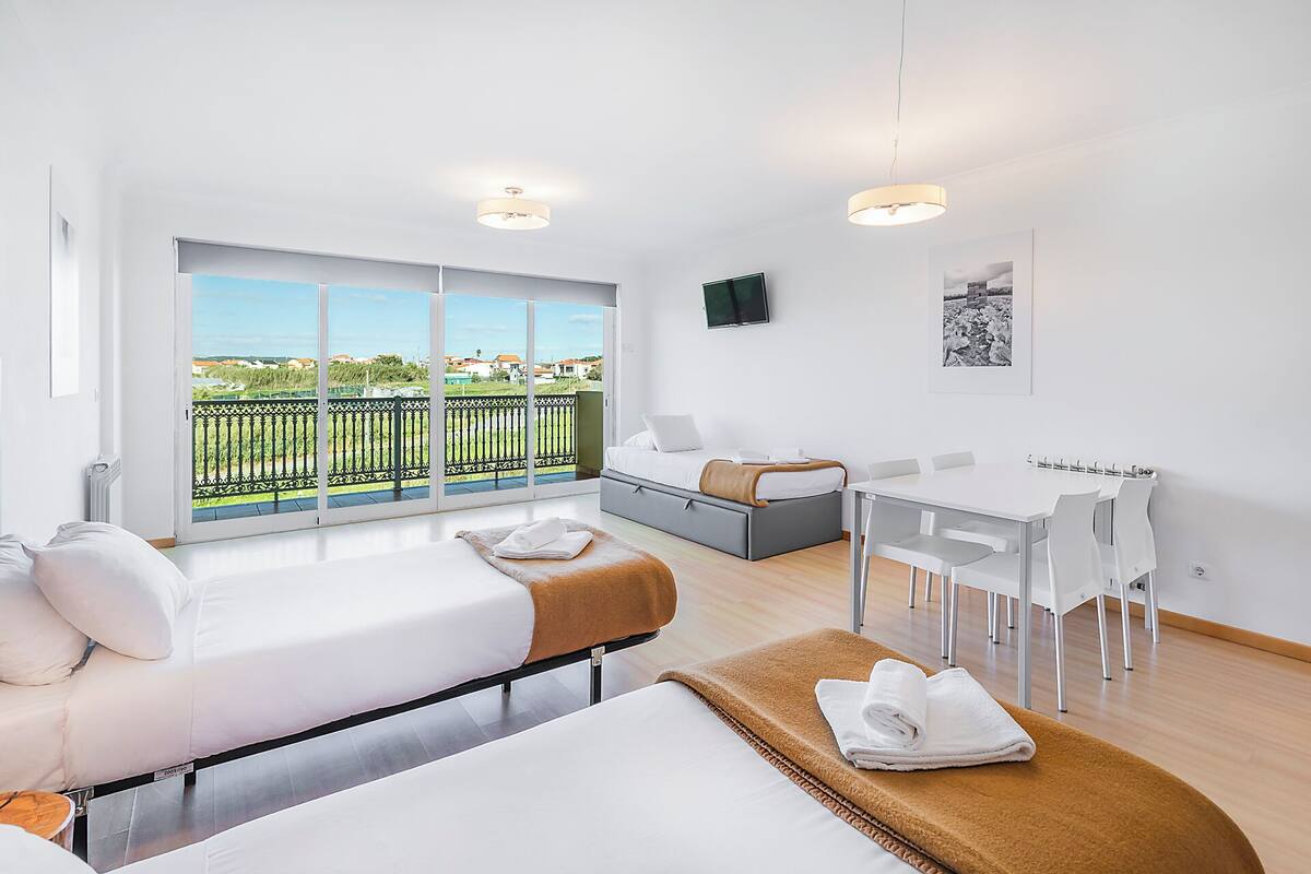 Una habitación de hotel moderna con balcón, cama, sofá, mesa de comedor y televisor.