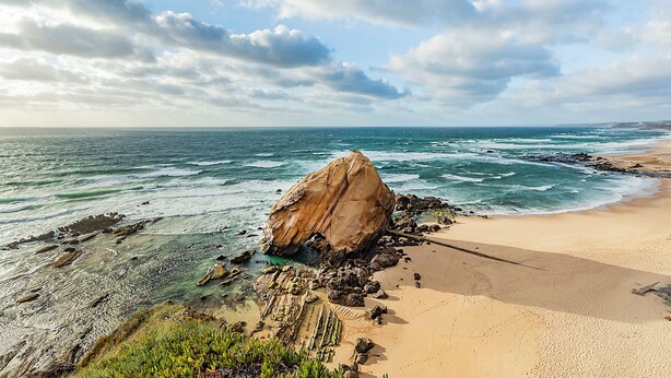A coastal landscape with a prominent rock formation, clear skies, and a sandy beach. - HI Santa Cruz - Pousada de Juventude - Hostel (Torres Vedras)
