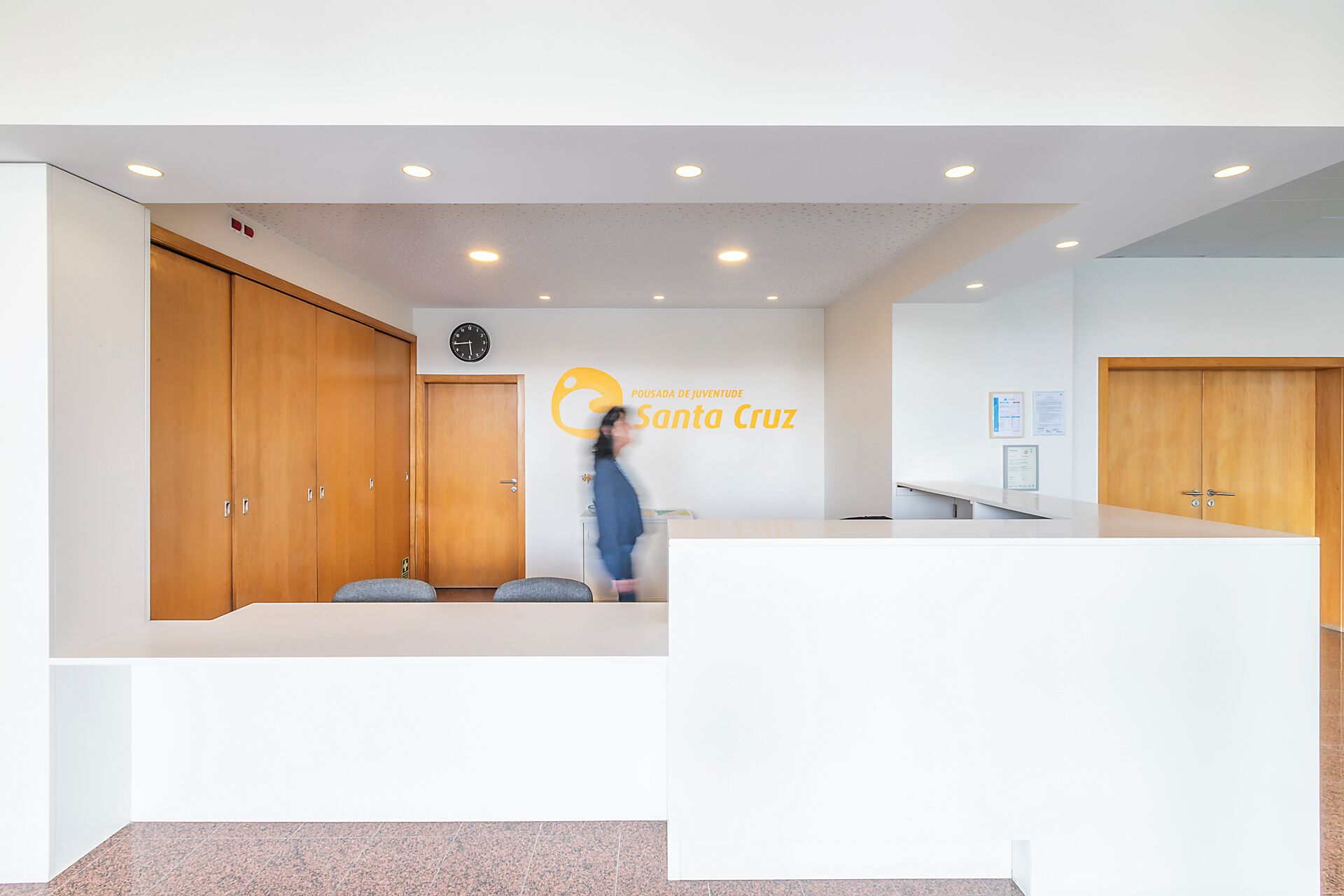 A reception area with a wooden door, a clock, and a logo on the wall.