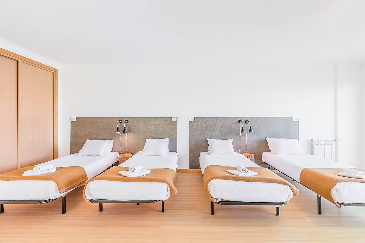 Habitación de hotel con dos camas individuales, cada una con cabecero de madera, ropa blanca y una manta marrón.