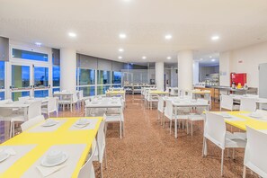 A spacious dining area with multiple tables and chairs, large windows, and a kitchen area in the background. - HI Santa Cruz - Pousada de Juventude - Hostel (Torres Vedras)