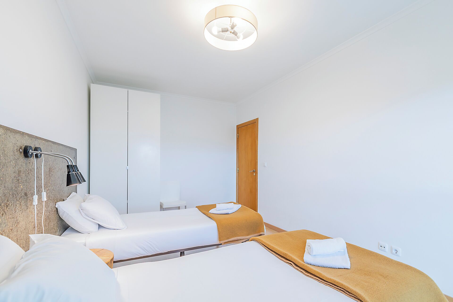 Ett hotellrum med två sängar, en trädörr, en takfläkt och en väggmonterad lampa.