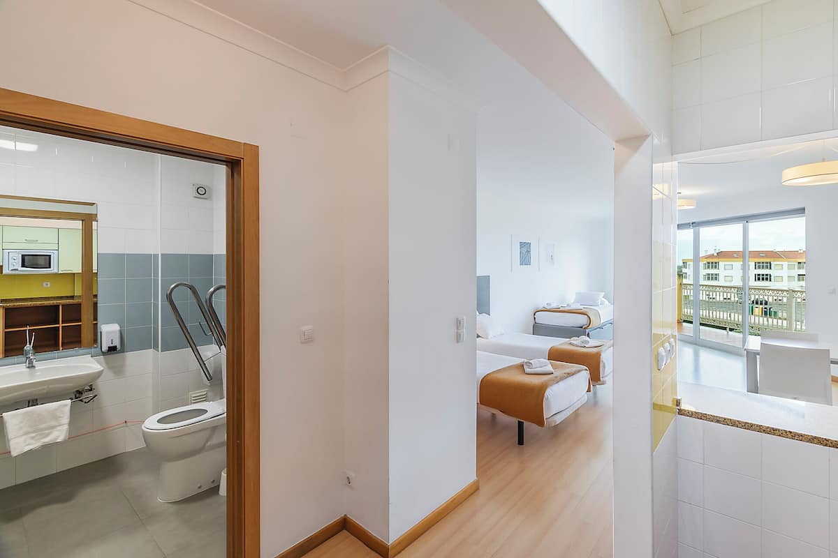 Una habitación de hotel con baño, cama, ventana con vistas y balcón.
