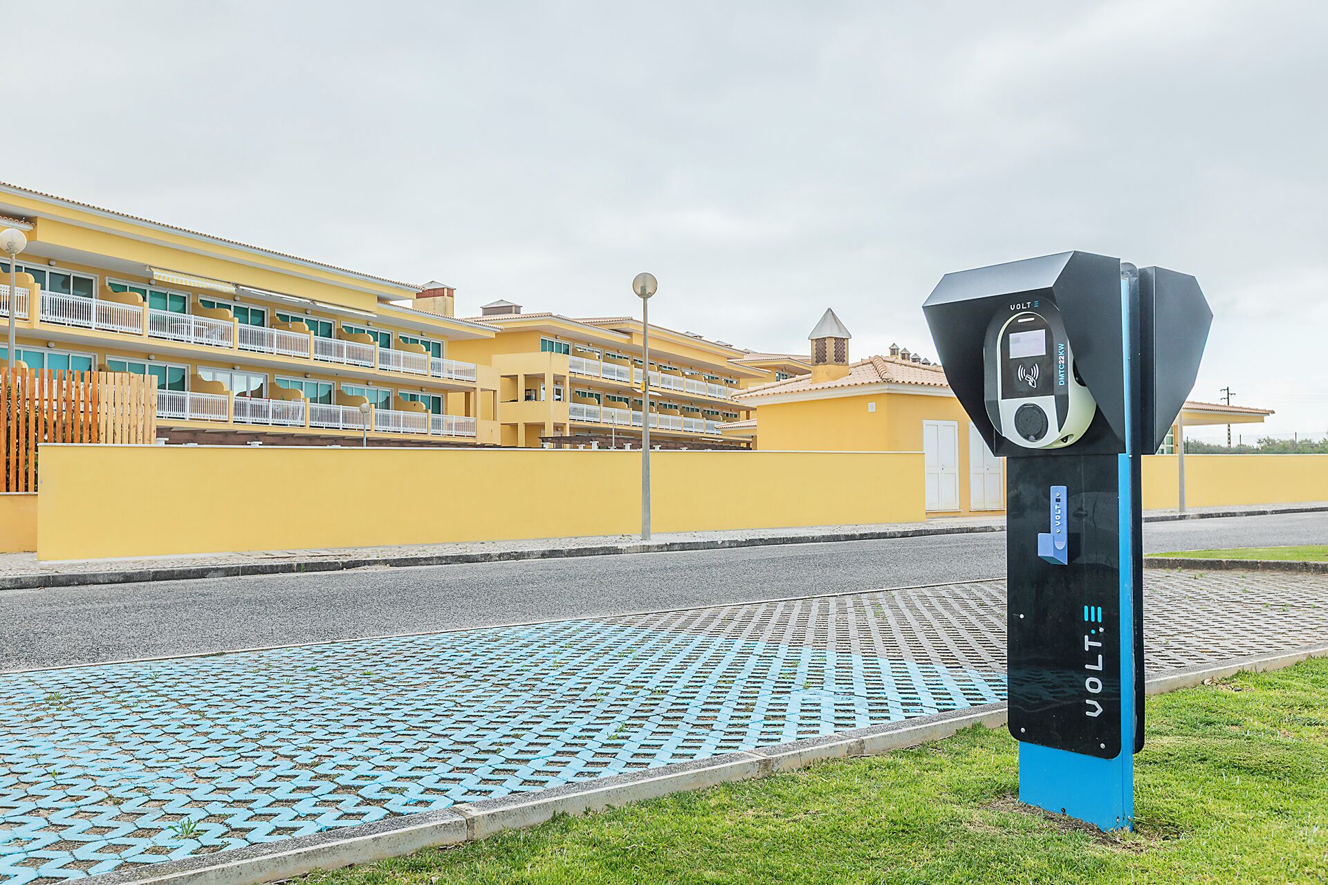 A parking meter with a digital display, a blue base, and a yellow building with balconies in the background.